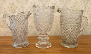 A Trio of Colorless Decorative Pressed Glassware Including Two Pitchers and a Footed Vase